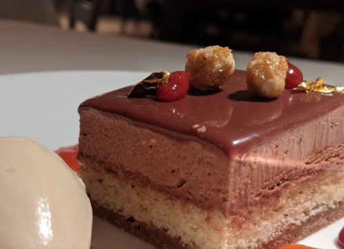 A decadent chocolate dessert layered with mousse, garnished with gold leaf, berries, and served with a scoop of ice cream.