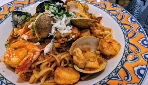 A colorful bowl of seafood pasta with shrimp, clams, mussels, and herbs on a decorative plate.
