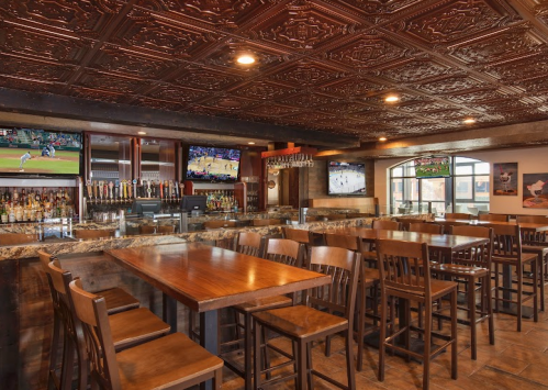 A cozy bar interior with wooden seating, a granite countertop, and multiple screens showing sports events.