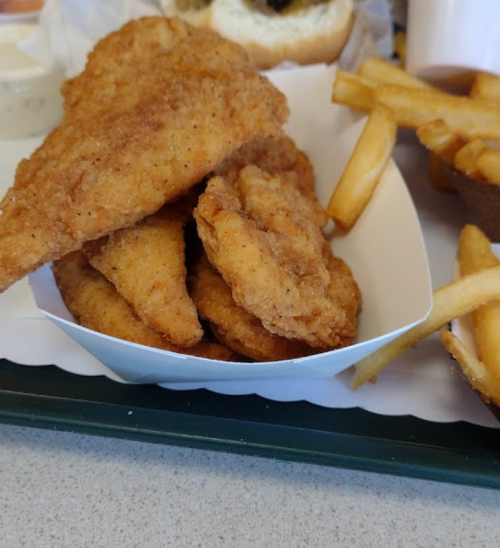 A serving of crispy fried chicken tenders in a white tray, accompanied by golden French fries.