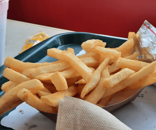 A tray of golden, crispy French fries with a napkin and a condiment packet in the background.