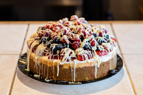 A delicious cheesecake topped with fresh raspberries, blueberries, and drizzled with white chocolate.