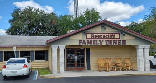 Exterior of Reececliff Family Diner, featuring a wooden sign, large windows, and a few rocking chairs on the porch.