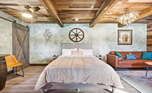 Cozy bedroom with a wooden ceiling, a bed, a leather sofa, and rustic decor elements.