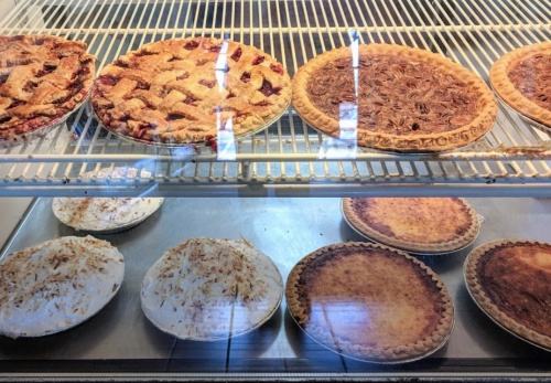 A display case filled with various pies, including cherry, pecan, coconut cream, and custard pies.