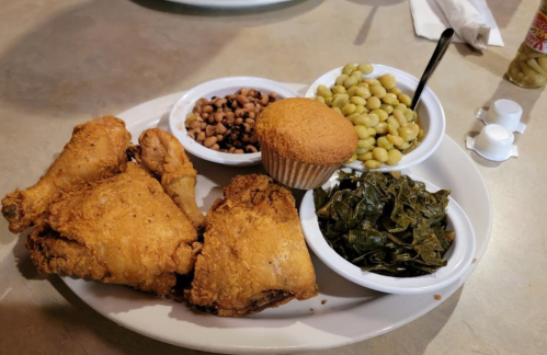 A plate of fried chicken with sides of black-eyed peas, green beans, collard greens, and a cornbread muffin.