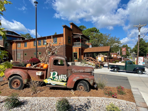 Rustic truck with pumpkins in front of Patti's Restaurant, surrounded by greenery and a blue sky with clouds.