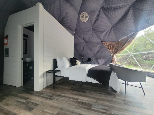 Cozy interior of a geodesic dome with a bed, chair, and modern decor, featuring a unique textured ceiling.