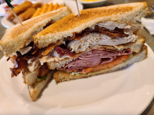A stacked sandwich with layers of turkey, ham, and bacon, served on toasted bread.