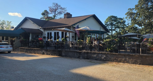 A charming restaurant with outdoor seating, surrounded by greenery and a gravel parking area.