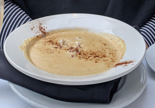 A creamy soup in a white bowl, garnished with a sprinkle of spices, served on a black napkin.