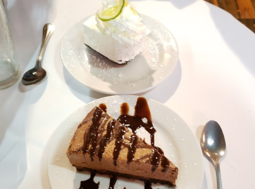 Two dessert plates: one with chocolate cheesecake drizzled in chocolate sauce, the other with a lime pie topped with whipped cream.