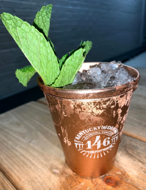 A copper cup filled with crushed ice and mint leaves, sitting on a wooden table.