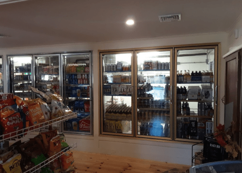 A convenience store interior featuring glass display coolers filled with beverages and snacks on a wooden counter.