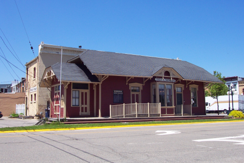 Historic red train station with a porch, set against a clear blue sky.