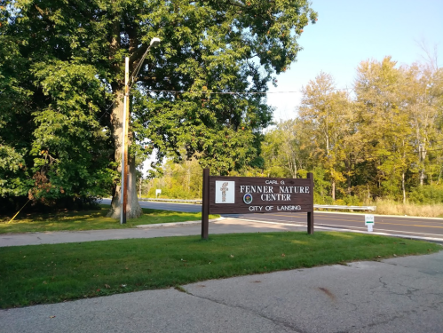 Sign for Carl G. Fenner Nature Center in Lansing, surrounded by trees and a clear blue sky.