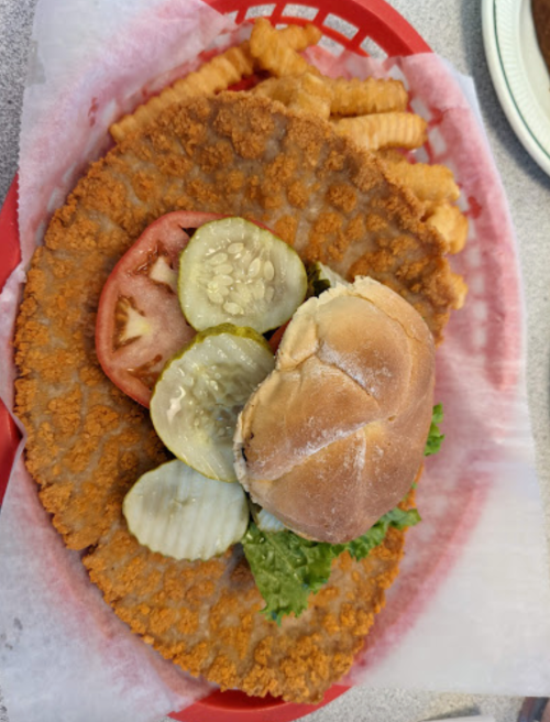 A large fried chicken sandwich with lettuce, tomato, pickles, and crinkle-cut fries in a red basket.