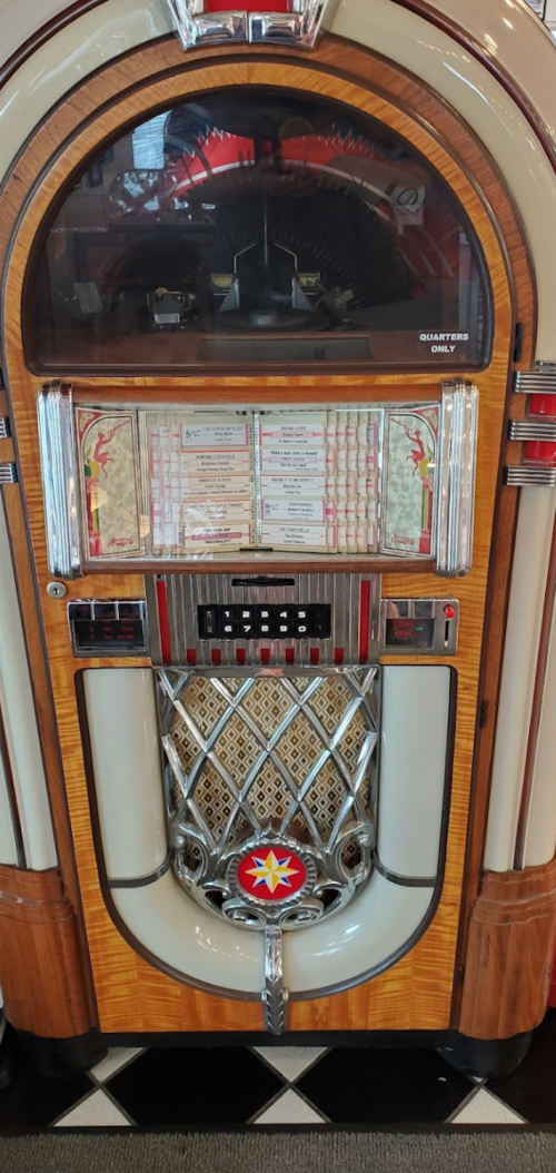 A vintage jukebox with a wooden finish, featuring a selection of songs and a coin slot for quarters.