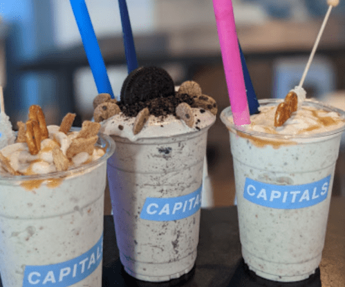 Three milkshakes topped with cookies, nuts, and colorful straws, labeled "CAPITALS."