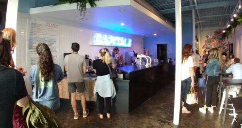 A vibrant ice cream shop with a long counter, customers ordering, and colorful decor in a bright, modern space.