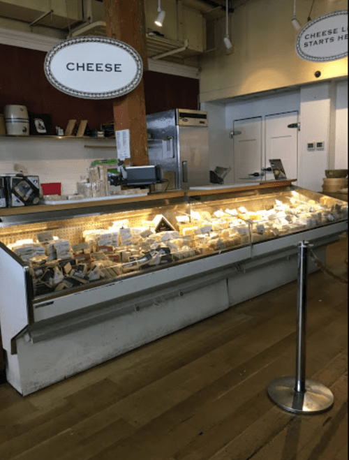 A cheese display case filled with various cheeses, labeled and neatly arranged, in a shop setting.