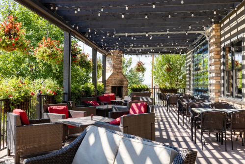A cozy outdoor patio with wicker furniture, red cushions, and hanging plants, illuminated by string lights.