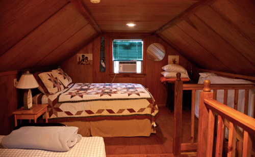 Cozy attic bedroom with wooden walls, a quilted bed, and a small window air conditioner.