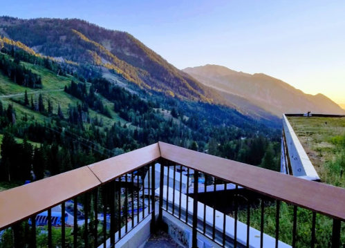 A scenic view from a balcony overlooking lush green mountains and a valley at sunrise.