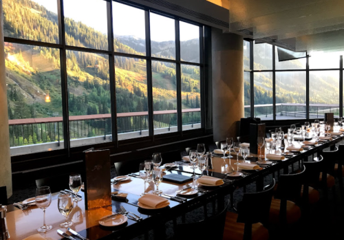 A dining area with a long table set for a meal, featuring large windows showcasing a mountain view.