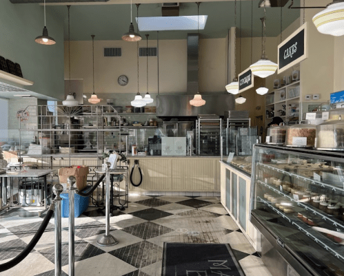 A cozy bakery interior with glass display cases, a counter, and pastel-colored walls, featuring various baked goods.