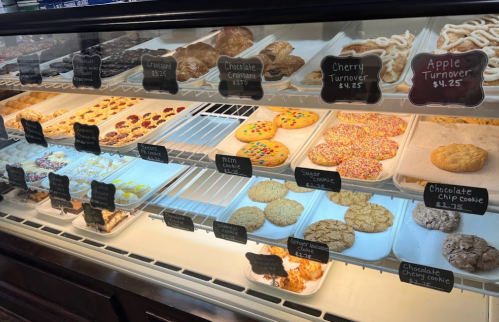 Display case filled with various baked goods, including cookies, croissants, and fruit turnovers, with price tags visible.