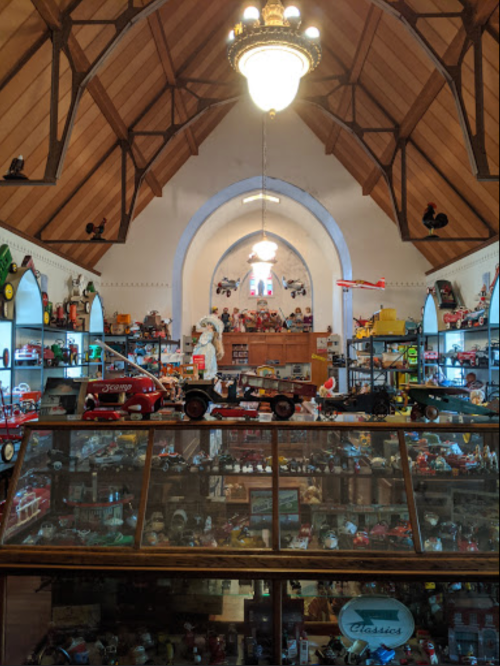 A vintage shop interior with a wooden ceiling, showcasing various collectibles and model cars in display cases.