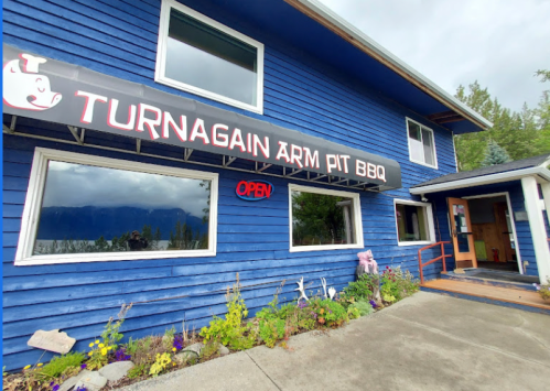 Exterior of Turnagain Arm Pit BBQ, a blue building with an "OPEN" sign and a welcoming entrance.