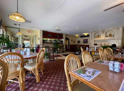 Cozy restaurant interior with wooden tables, rattan chairs, and decorative plants, creating a warm atmosphere.
