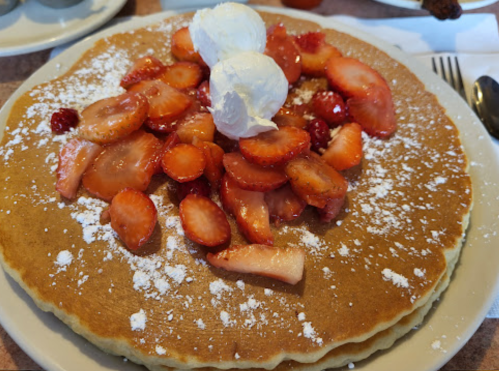 A large pancake topped with sliced strawberries and whipped cream, dusted with powdered sugar.