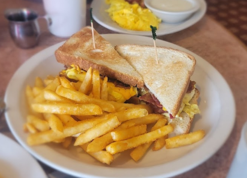 A sandwich with bacon and cheese, served with a side of golden French fries on a white plate.