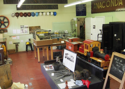 A museum display featuring model trains, mining artifacts, and historical signs in a well-lit room.