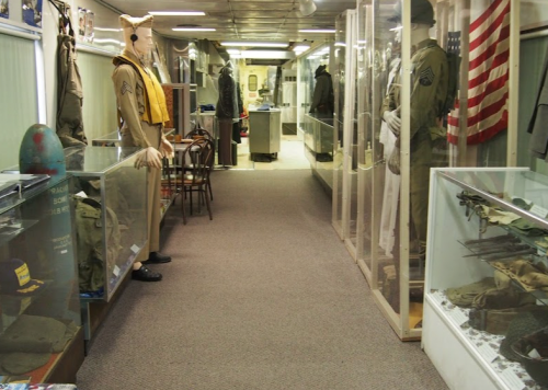 A museum hallway lined with display cases featuring military uniforms, artifacts, and an American flag.