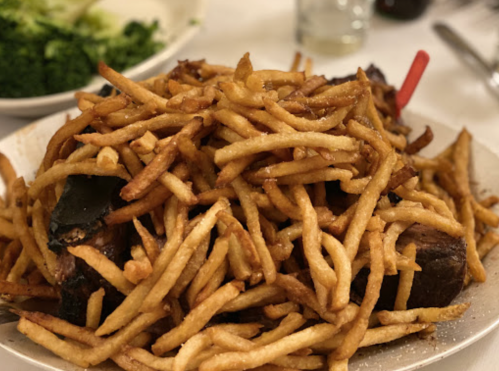 A large plate of crispy golden French fries piled over a serving of meat.