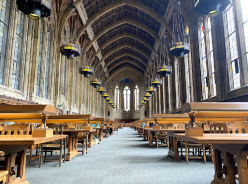 A spacious, historic library interior with tall ceilings, large windows, and rows of wooden study tables.