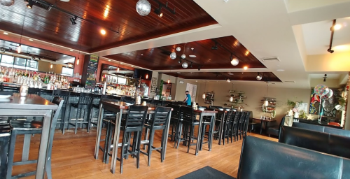 A spacious restaurant interior with wooden floors, bar area, and tables, featuring hanging disco balls and a staff member.