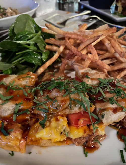A plate of enchiladas topped with sauce and herbs, served with fries and a side of fresh spinach.
