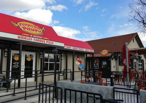 Exterior of Flying Pie Pizzeria with a red awning, outdoor seating, and a cartoon character on the wall.