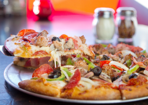 A close-up of a pizza topped with pepperoni, olives, green peppers, and cheese, with a slice being lifted.