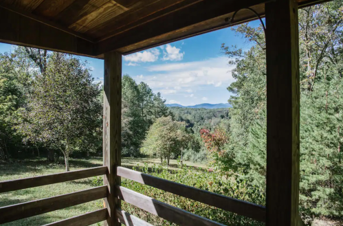 View from a wooden porch overlooking a lush green landscape and distant mountains under a blue sky.