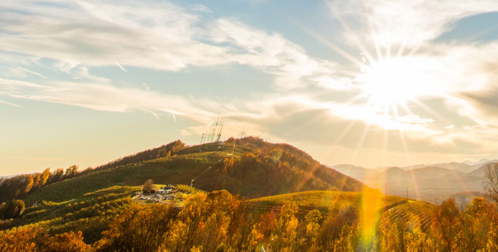 A sunlit landscape with rolling hills, autumn foliage, and communication towers against a clear sky.
