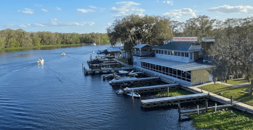 A scenic view of a river with boats, docks, and a restaurant along the shore under a clear blue sky.