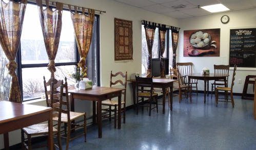 Cozy café interior with wooden tables, chairs, decorative curtains, and a wall art featuring cookies.
