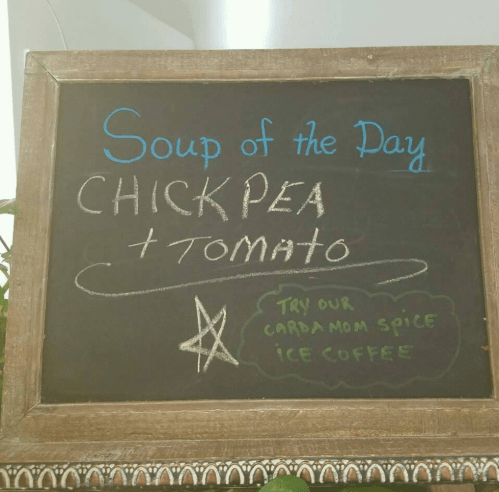 Chalkboard sign displaying "Soup of the Day: Chickpea + Tomato" and promoting cardamom spice iced coffee.