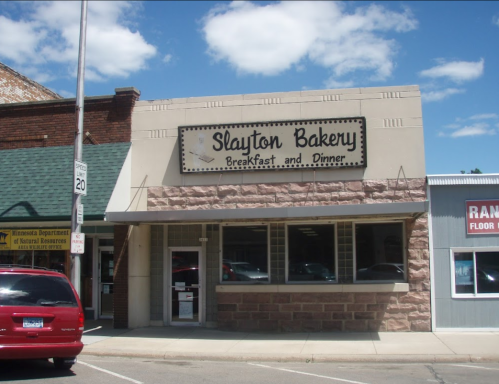 Exterior of Slayton Bakery, featuring a sign that reads "Breakfast and Dinner," with a clear blue sky above.